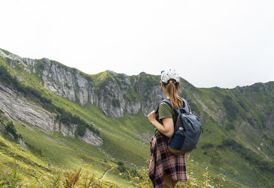 Young woman hiker in cap with backpack looking at mountain view in summer healthy active lifestyle