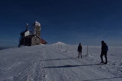 People walking on snow covered field against sky