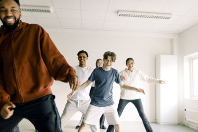 Smiling boy learning to dance with friends and teacher in studio at high school