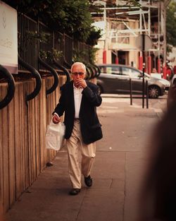 Senior man smoking cigarette while walking on sidewalk in city