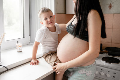 Midsection of pregnant mother with son in kitchen