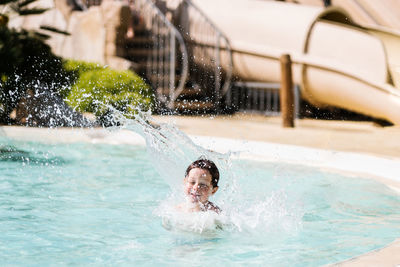 Happy shirtless little boy jumping into outdoor swimming pool during summer holidays and having fun