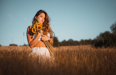 Young woman standing on field against sky