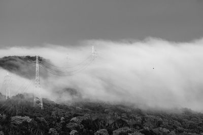 Electricity pylons on field against sky during foggy weather