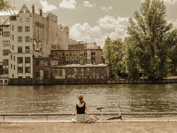 Woman sitting by river against sky