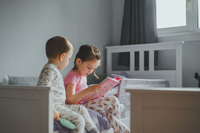 Young girl reading a story book to her brother before bedtime