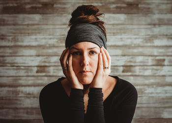 Portrait of woman with face resting in hands against wooden background