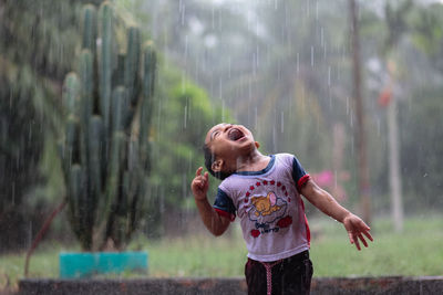 Full length of happy boy splashing water in rain