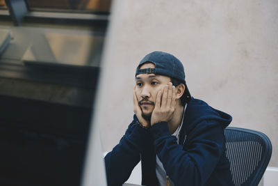 Portrait of young man looking away against wall