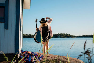 Woman walking on a rock whilst holding a guitar smiling in the sun