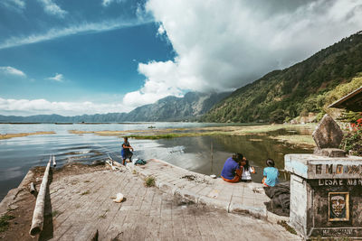 People sitting on mountain by lake against sky
