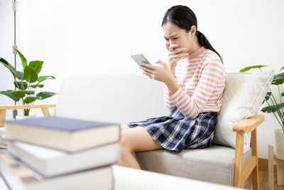 Young woman using mobile phone while sitting on sofa at home