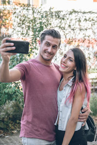 A portrait of brunette young couple smiling and taking selfie photo while walking outdoors
