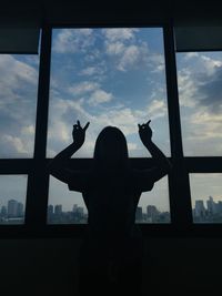 Rear view of silhouette woman looking through window