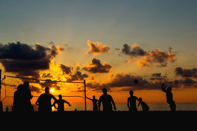 Silhouette people playing volleyball at beach during sunset