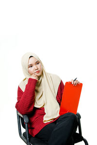 Young woman sitting on seat against white background