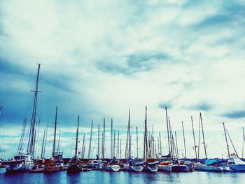 Sailboats moored at harbor against cloudy sky