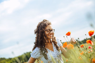 Smiling woman looking at flowers against sky