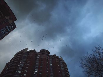 Low angle view of birds flying against cloudy sky