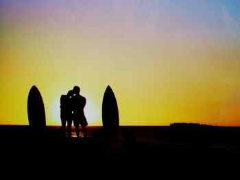 Silhouette friends standing on shore against sky during sunset