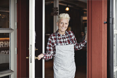 Portrait of smiling confident manual worker standing at doorway by restaurant