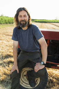 Smiling mature man sitting on tire of tractor at farm