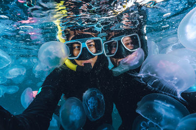 Two people are underwater with jellyfish surrounding them. 