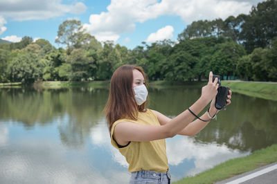 Side view of woman with arms raised standing against lake