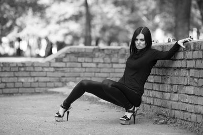 Full length portrait of woman sitting against brick wall