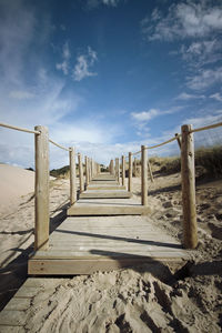 Wooden railing on beach against sky