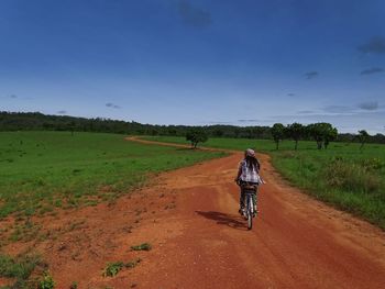 Rear view of woman riding bicycle on dirt road