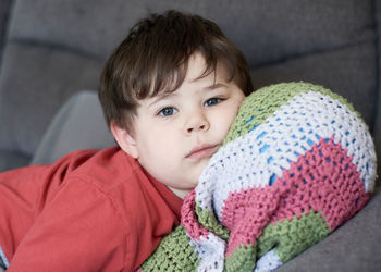 Portrait of a young boy resting on the couch with his head on a ball inside his blanket