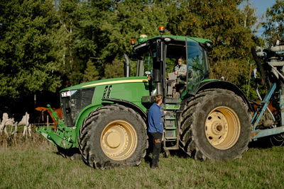 Farmer sitting in tractor and discussing with man standing at filed on sunny day