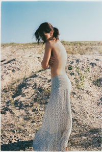 Full length of shirtless young woman standing on beach