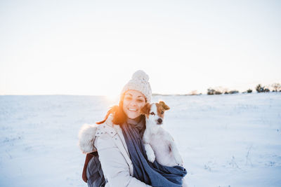 Portrait of smiling woman with dog on snow covered land against sky