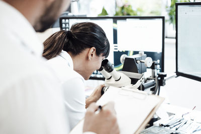Businesswoman looking through microscope by male colleague at laboratory
