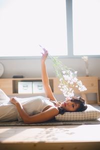 Portrait of woman holding flowers while lying at home