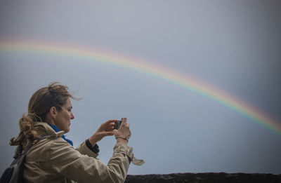 Woman photographing rainbow against sky