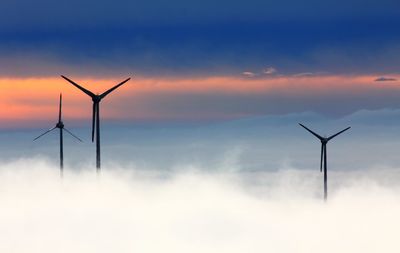 Wind turbines on field against sky during sunset