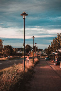 Street light by walkway in city against sky