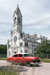 Cuba, havana, red vintage car parked in front of white painted church in la vibora neighborhood