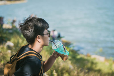 Young man having drink by sea