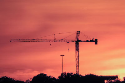Silhouette crane and trees against cloudy sky during sunset