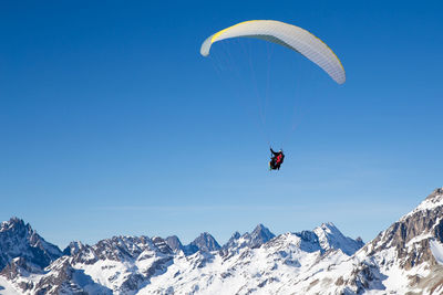 Person paragliding over snowcapped mountain against sky