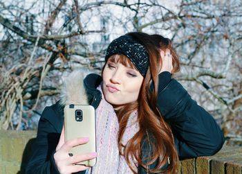 Woman taking selfie against bare trees