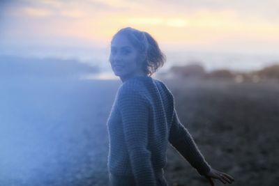 Portrait of happy young woman standing on field during sunset