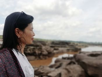 Young woman looking away while standing on beach against sky