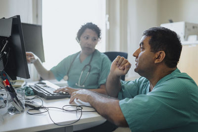 Male and female doctors discussing over computer at desk in hospital