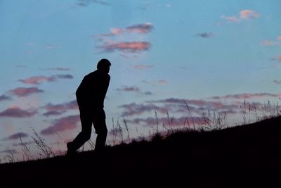 Silhouette man walking on field at sunset