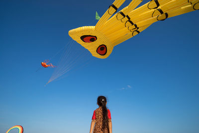 Low angle view of girl looking at kites flying in clear blue sky during festival